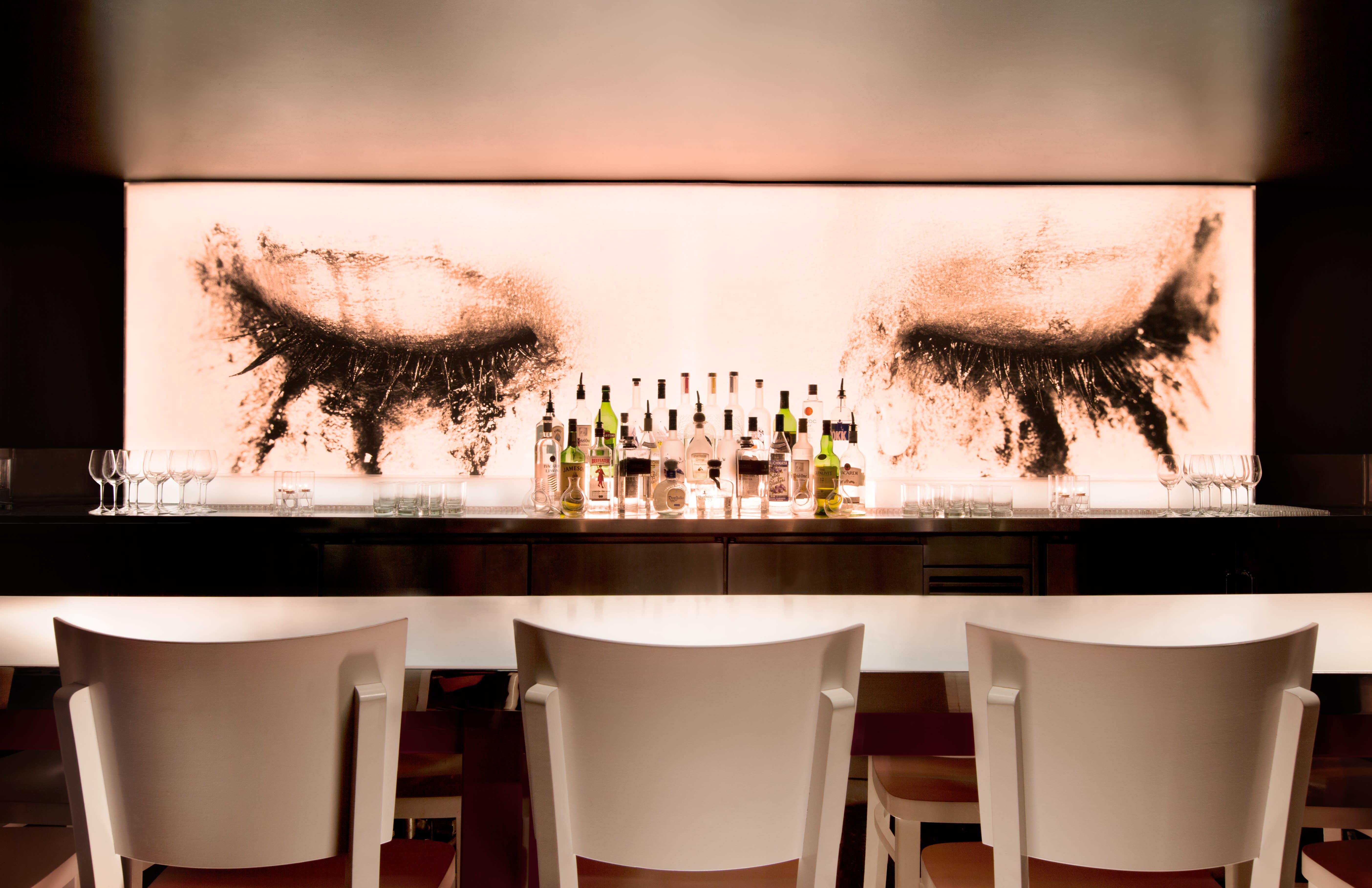 bar avec trois chaises blanches avec bar et peinture murale avec des yeux et du mascara taché