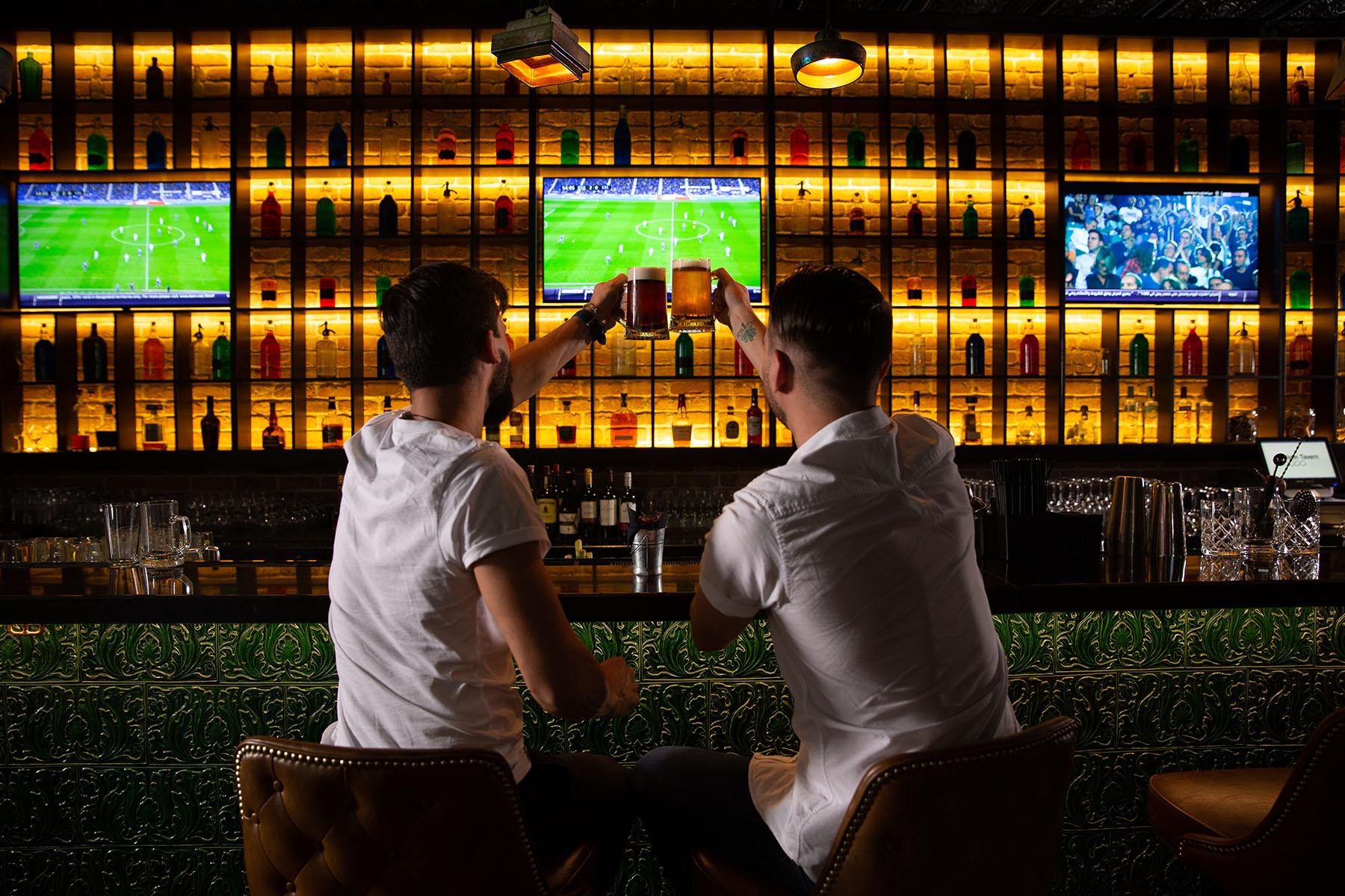 Des hommes acclament au bar avec un match de football en arrière-plan