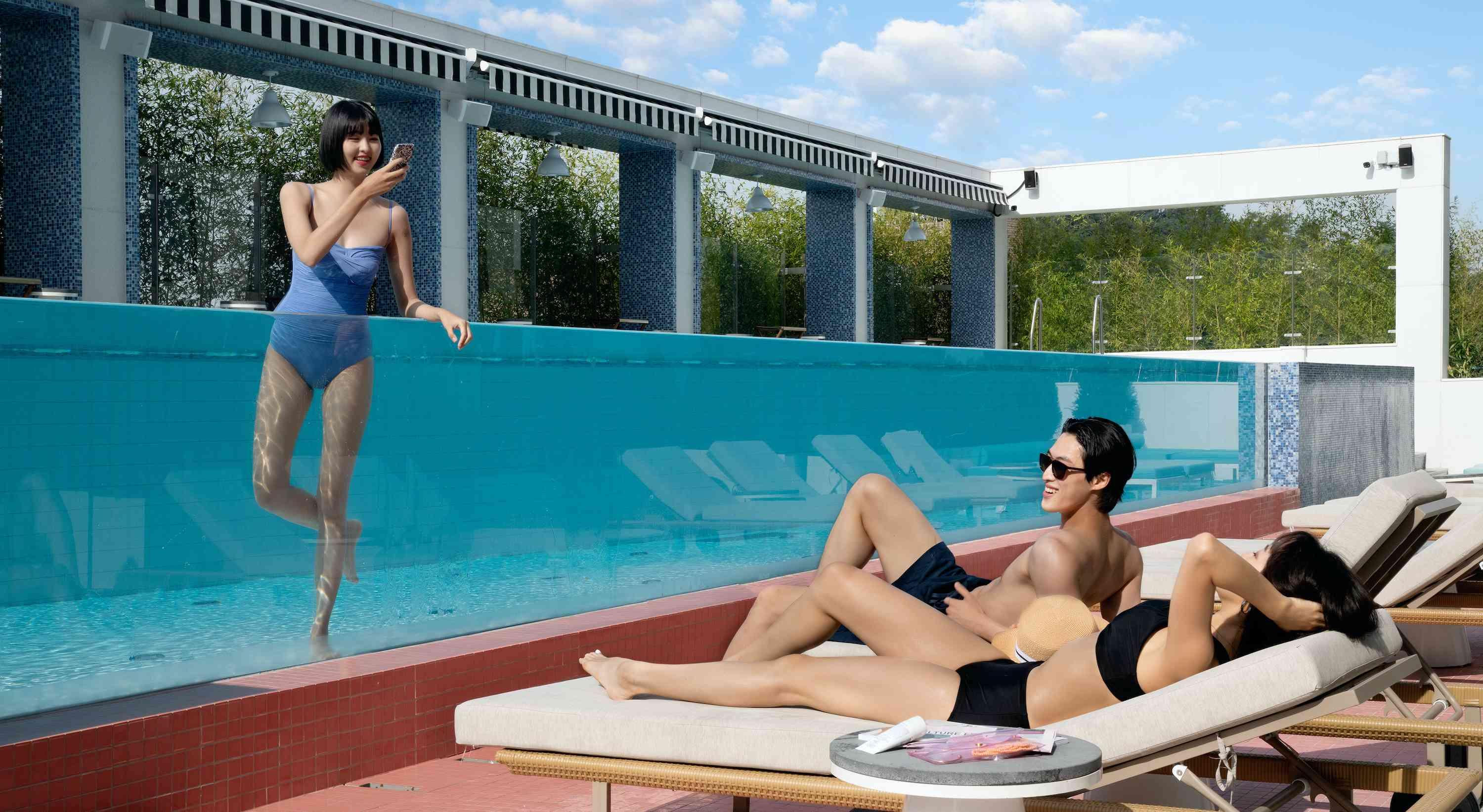 couple dans des chaises longues au bord d'une piscine avec un ami dans la piscine