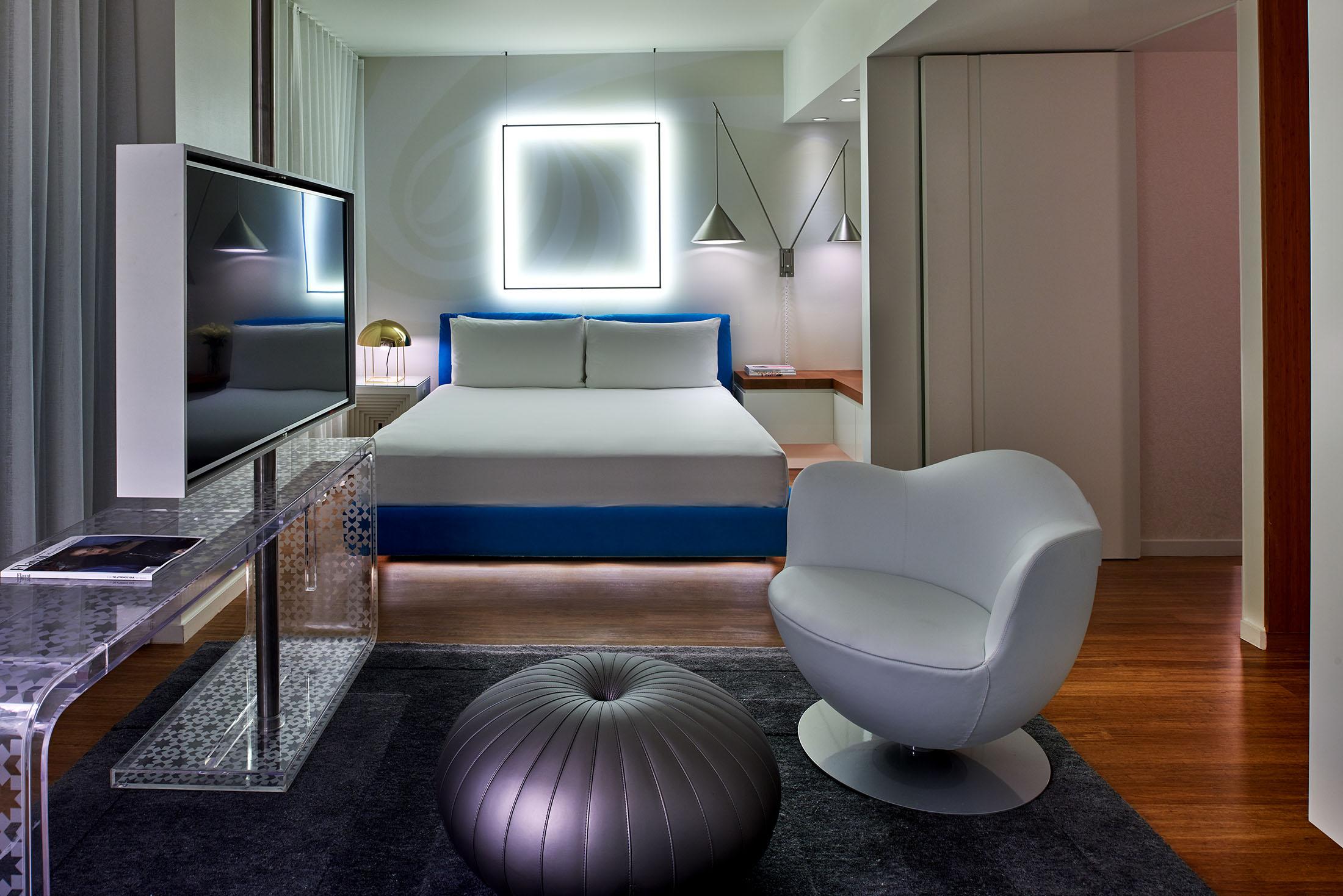 Chambre d'hôtel avec une lumière carrée derrière le lit et une chaise au premier plan.