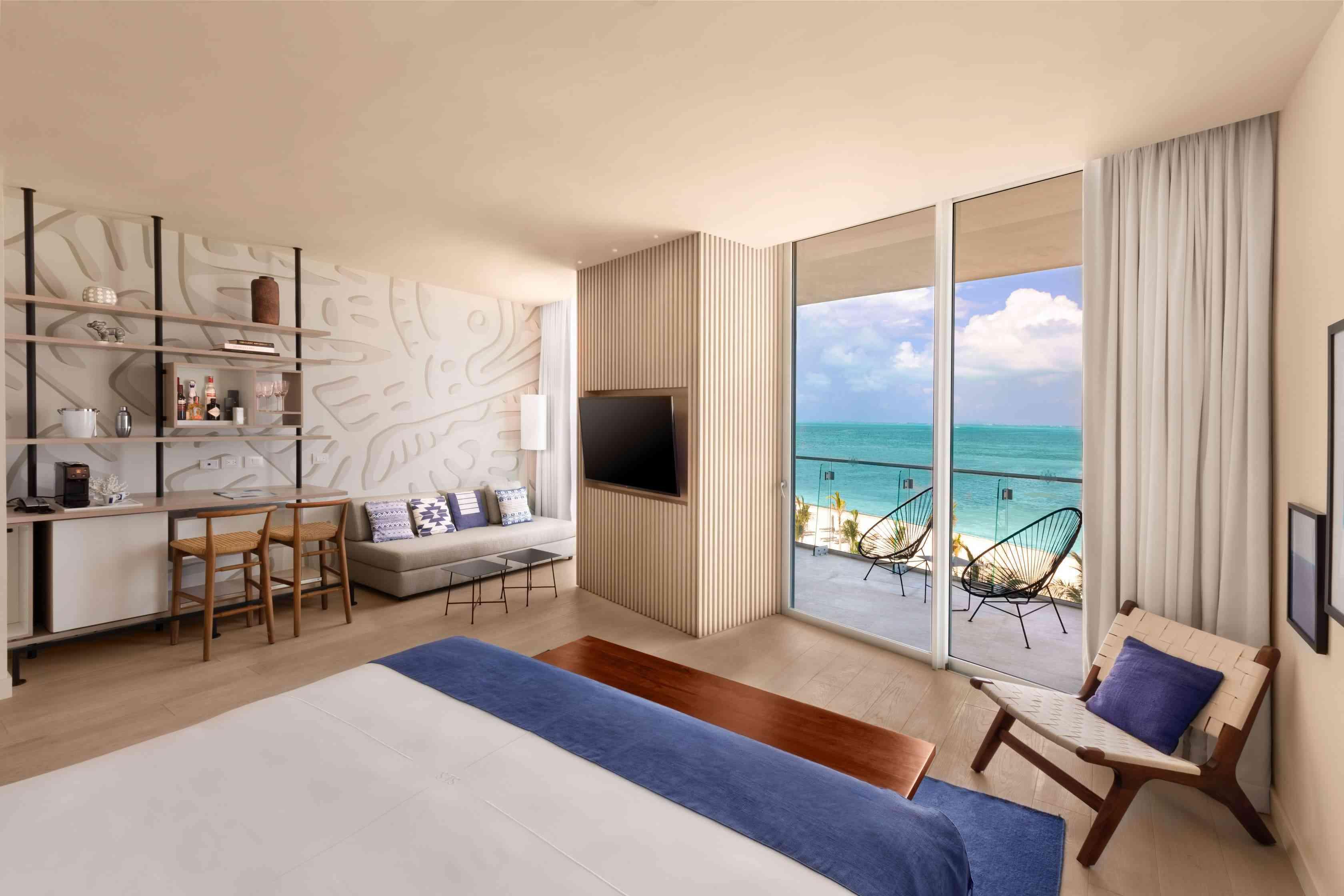 Plan large de la chambre lit king-size de luxe face à l'océan qui comprend un bureau, un coin salon, une télévision et un balcon avec vue sur l'océan