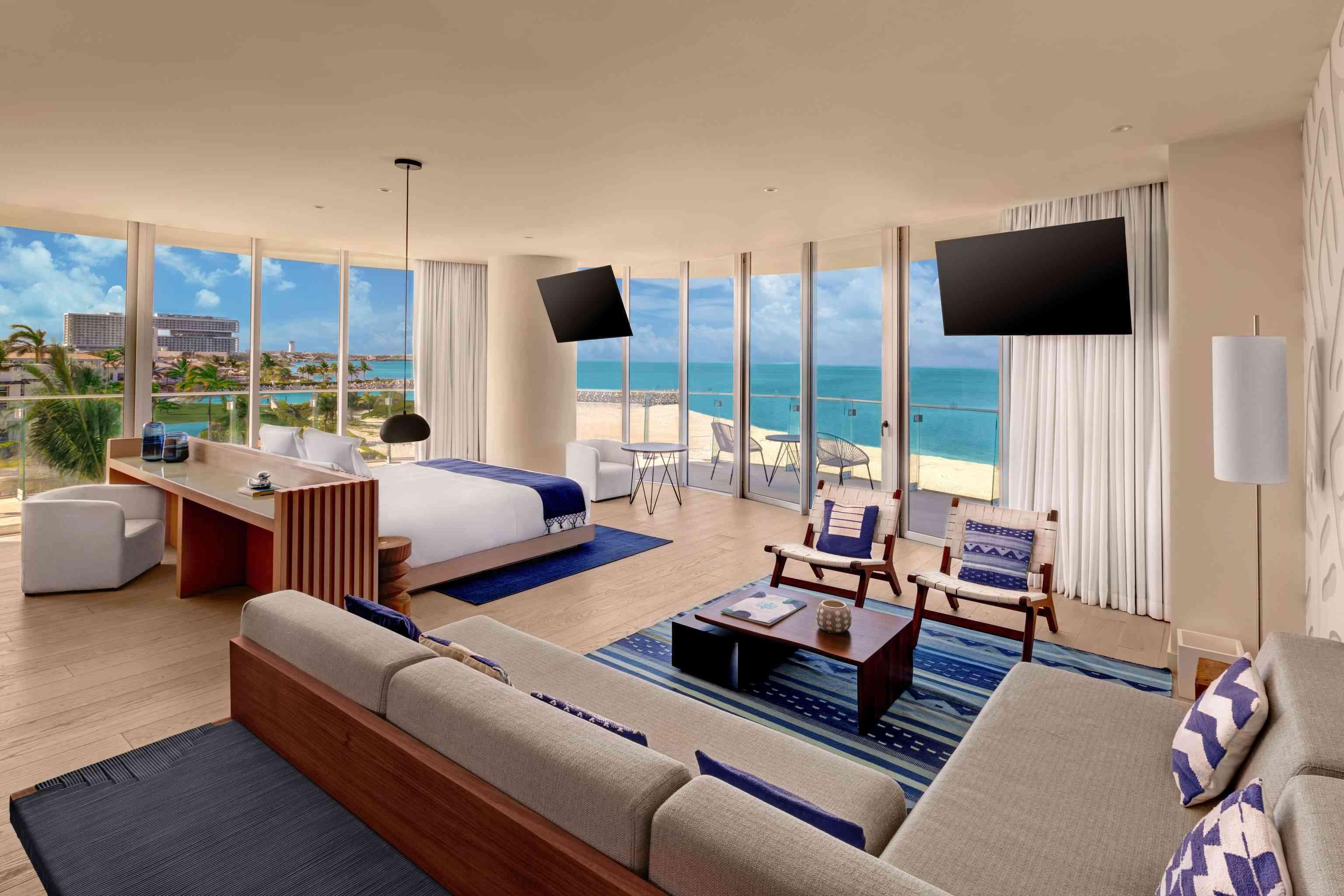Plan large de la suite Premier Ocean Front à une chambre qui comprend un bureau, un grand coin salon, 2 télévisions, un lit et un balcon avec vue sur l'océan