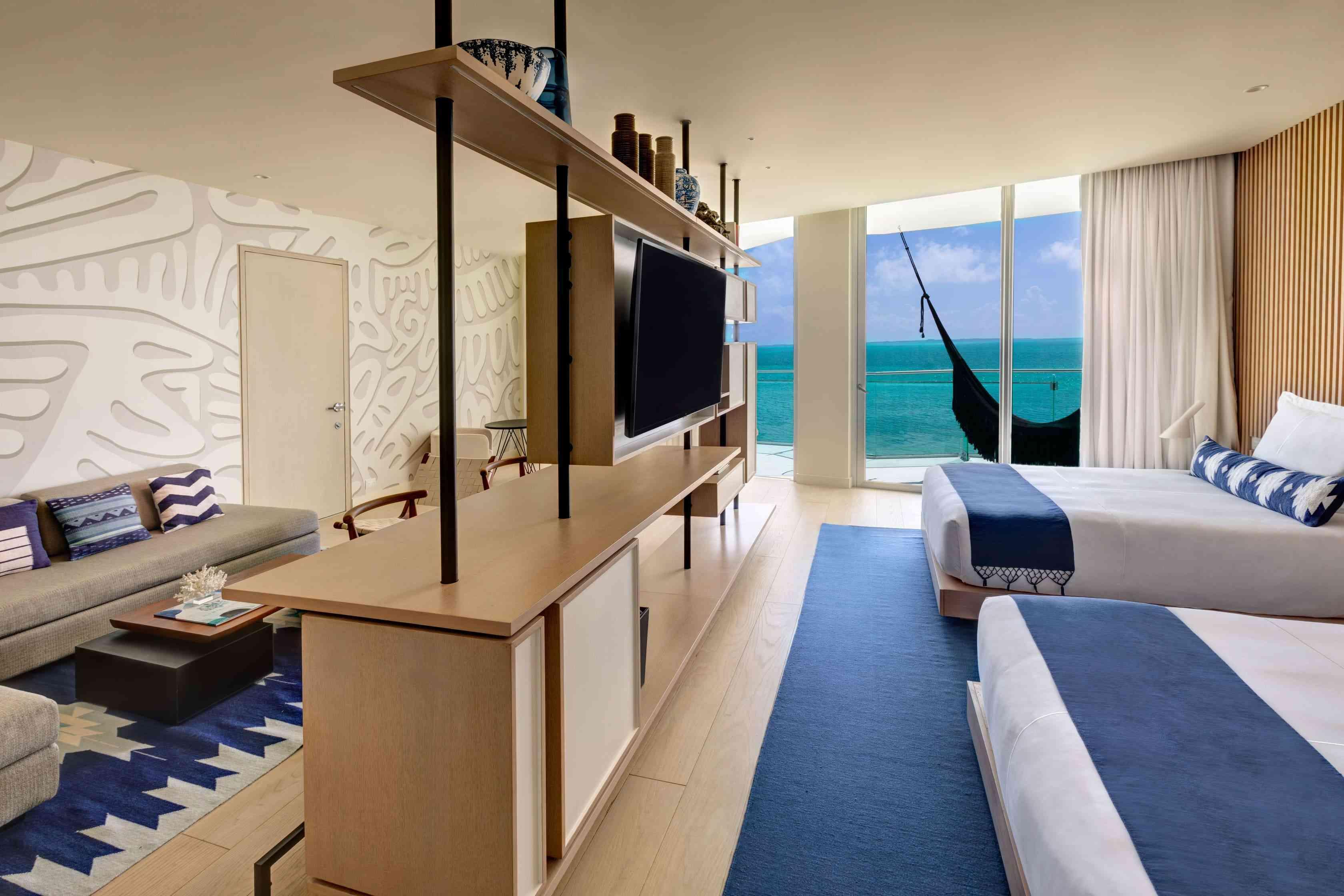 Photo de la suite de luxe à une chambre face à l'océan qui comprend deux lits doubles, une télévision, un bureau qui sépare la chambre du salon et un balcon avec un hamac donnant sur l'océan